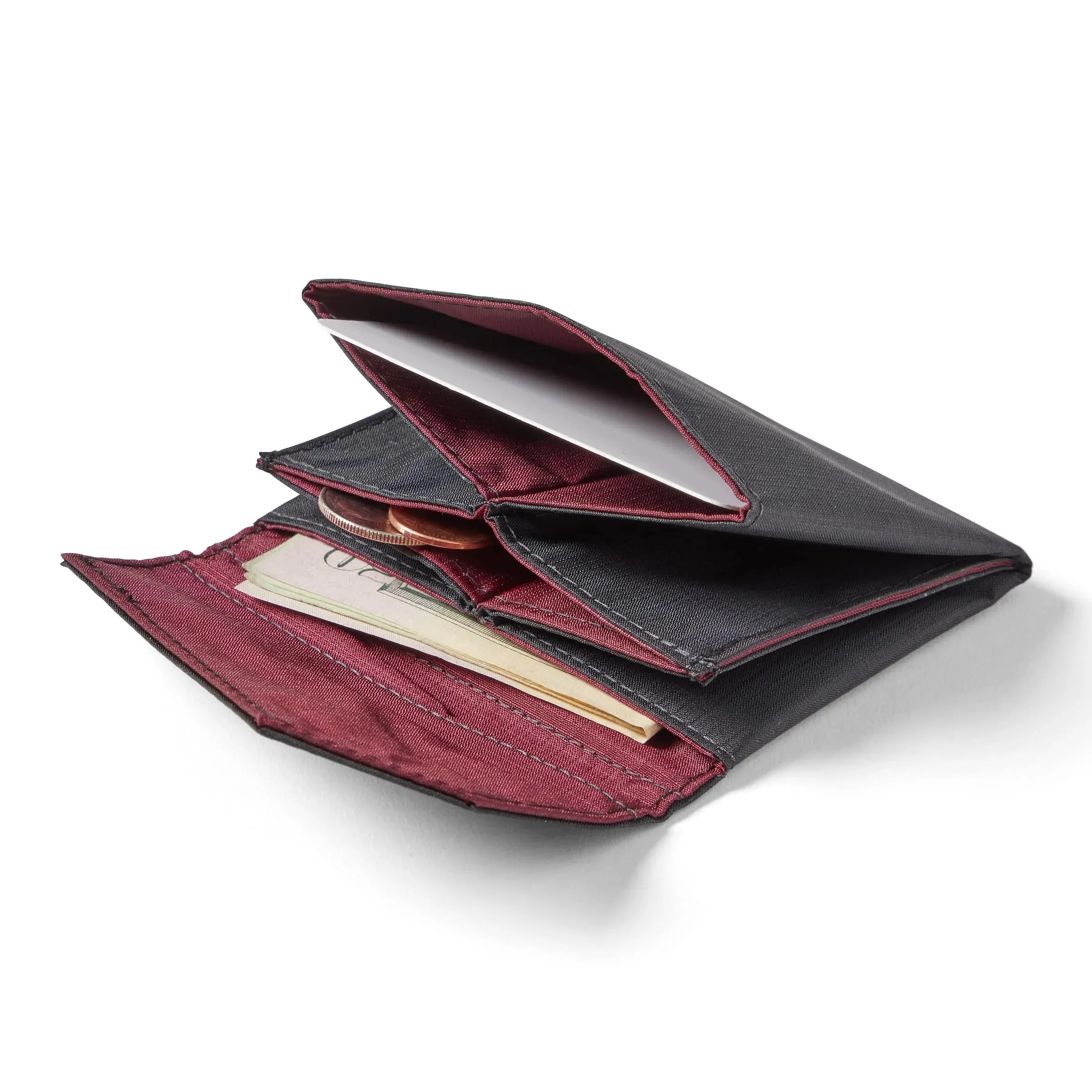 Allett's jet black ripstop nylon accordion wallet spread flat on a white surface, with coins and bills peeking out from the pockets. Allett Accordion Wallet in RFID Blocking Nylon jet-black