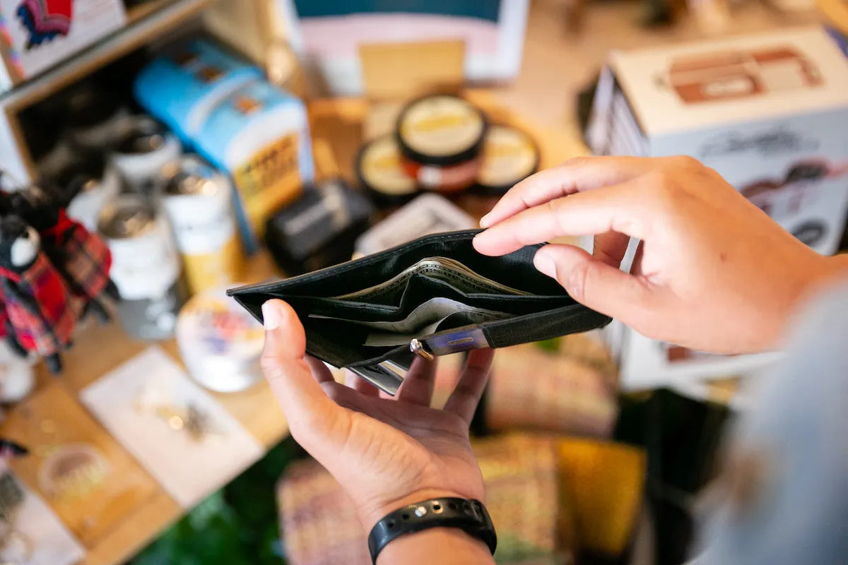Photo is of a black wallet opened with two pockets for cash showing within the wallet. Both wallets are holding dollar bills of different numbers.