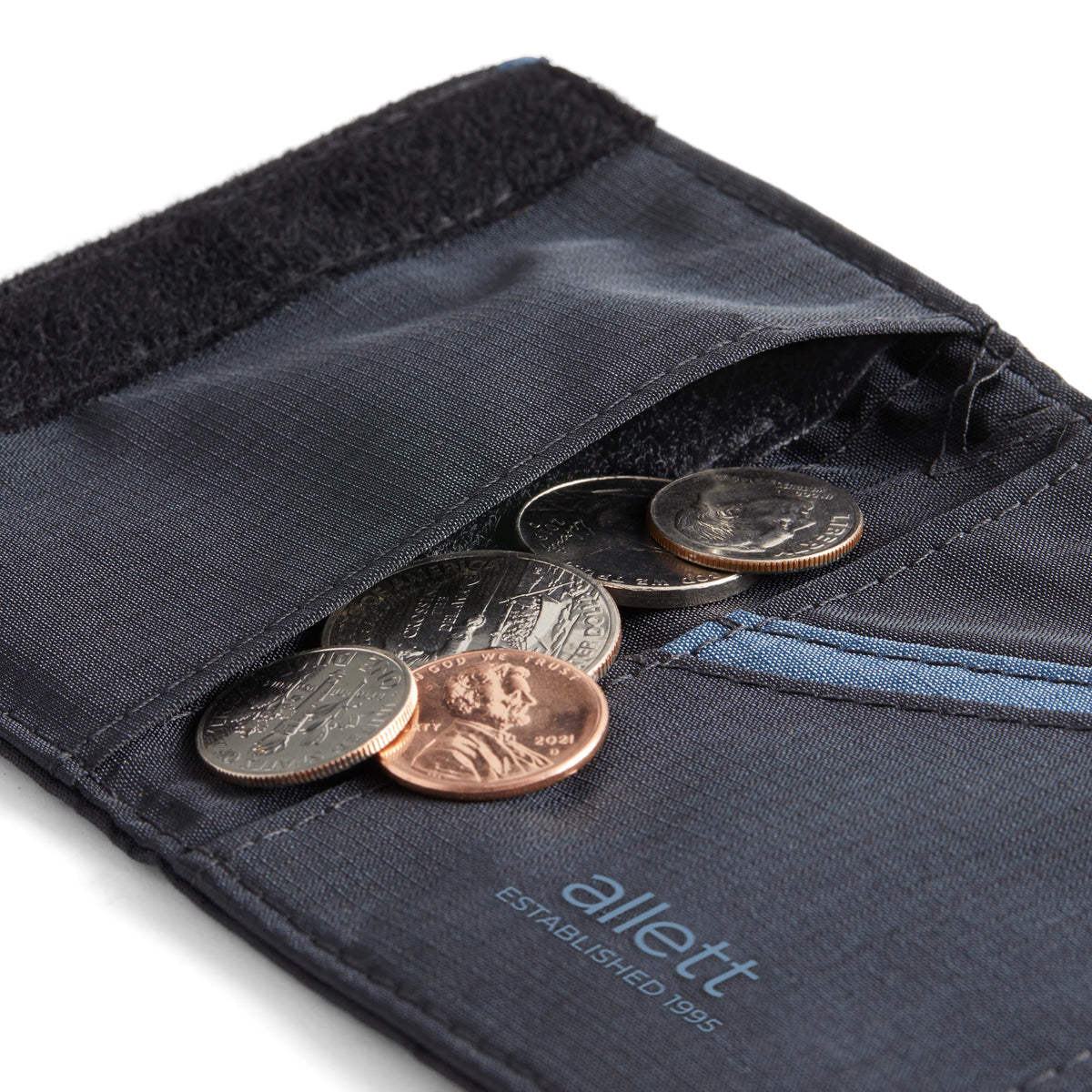 Various coins coming out of the internal coin pocket underneath the velco side pocket of the trifold wallet from Allett. Allett Trifold Wallet nylon edition - jet-black